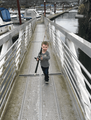 Young boy playing with tripod on walkway by marina