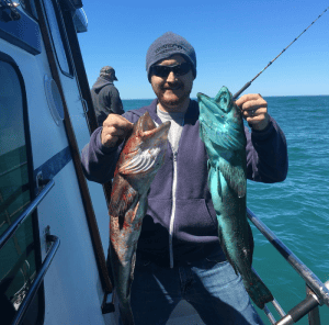 Man proudly holding two fish on a boat