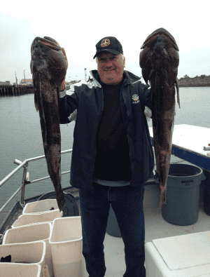 Man holding two large fish on boat deck.