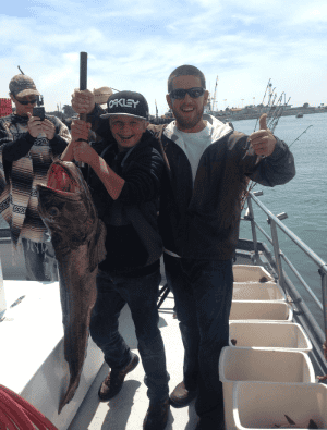 Two men smiling with a caught fish on boat.