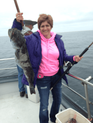 Woman in pink shirt proudly holding large fish on boat