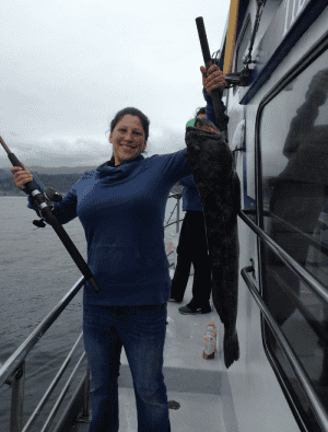 Woman proudly holding large fish on boat
