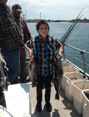 Boy holding large fish on boat deck
