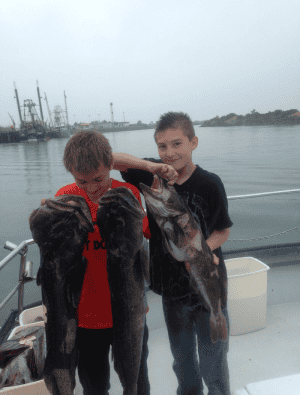 Two boys holding large fish on a boat