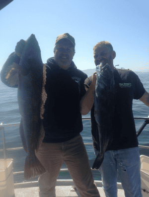 Two men holding large fish on boat deck.