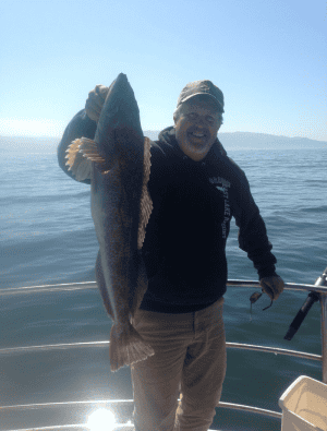 Smiling person holding large fish on boat